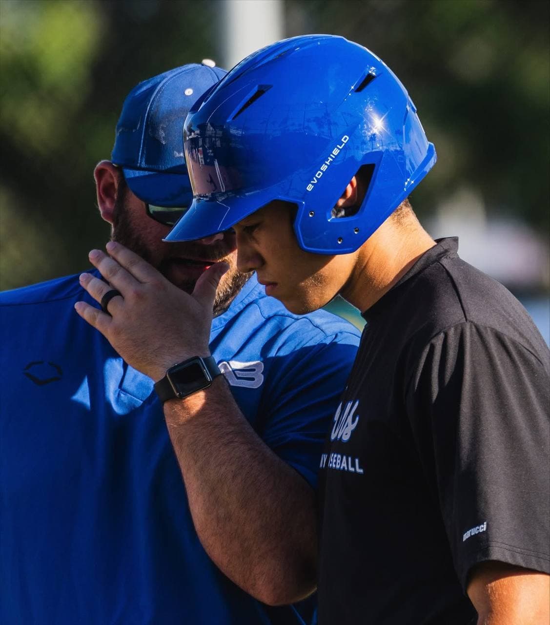 A coach talks through an at-bat with a helmeted A3 player