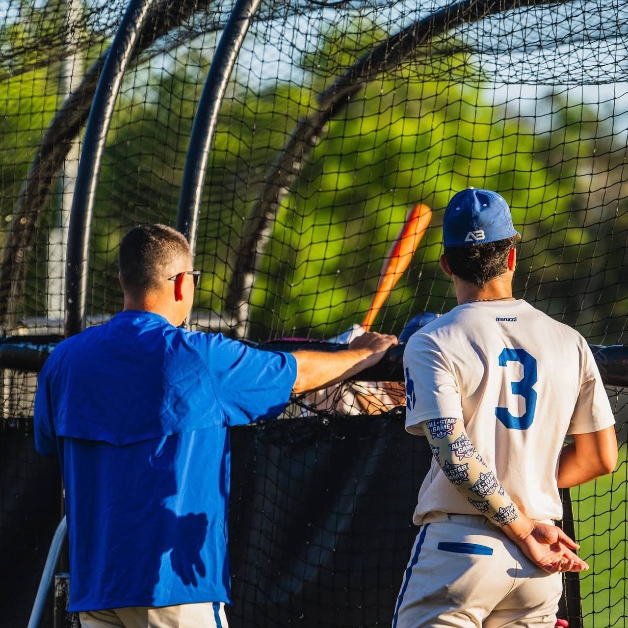 A coach runs batting practice in the outdoor cage